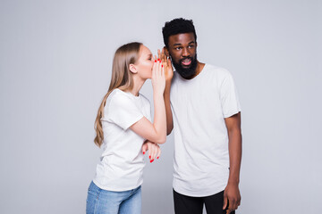 Young mixed couple telling secret each other isolated on white background