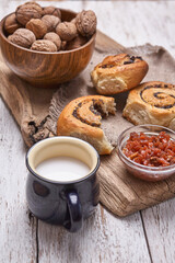Basket of homemade buns with jam, served on old wooden table with walnuts and cup of milk