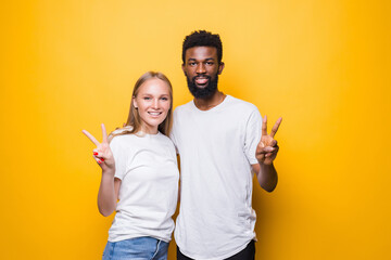 Young diverse couple peace gesture isolated on yellow background