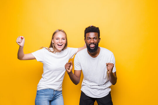 We are the champions. Joyful interracial couple rejoicing success, raising fists, celebrating victory, posing together over yellow background