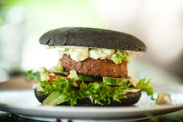 Vegan burger. Black bun, tofu-avocado salad, mayonnaise, cucumber, tomato, fresh salad. Delicious healthy hamburger food closeup served on a table for lunch in modern cuisine gourmet restaurant.