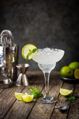 Cocktail margarita garnished with lime and mint on wooden background