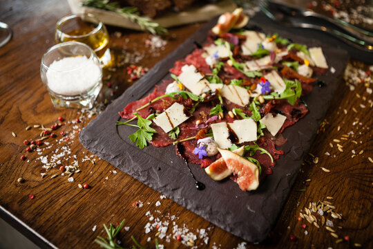 Beef carpaccio with pepper, rucola and parmesan served on a board. Delicious healthy Italian traditional antipasti snacks food closeup served for lunch with wine in modern gourmet cuisine restaurant