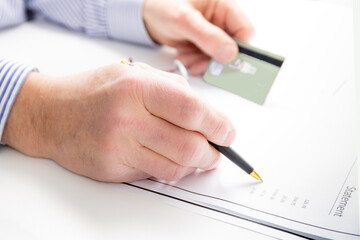 a man holds his credit card and checks his statement with a pen on a white background