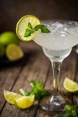Cocktail margarita garnished with lime and mint on wooden background