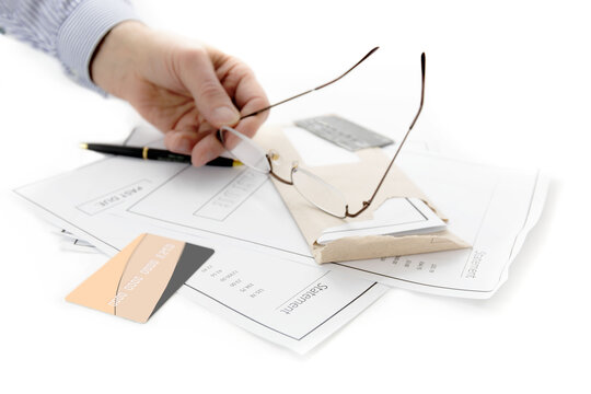 A Man's Hand Holds His Glasses Over A Stack Of Past Due Credit Card Bills Isolated On White