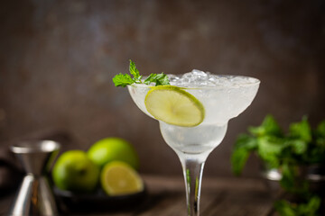 Cocktail margarita garnished with lime and mint on wooden background