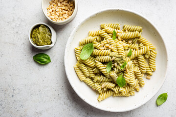 Italian Fussili pasta with basil pesto and fresh basil on white stone background. Top view.