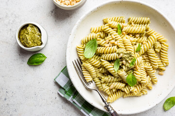 Italian Fussili pasta with basil pesto and fresh basil on white stone background. Top view.