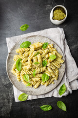 Italian Fussili pasta with basil pesto and fresh basil on black background. Top view.