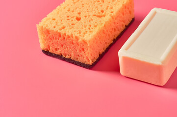 Brick of soap near sponge on pink background. Hygiene and cleaning concept