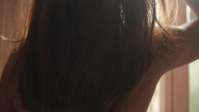 Naked woman playing with her hair in front of the window