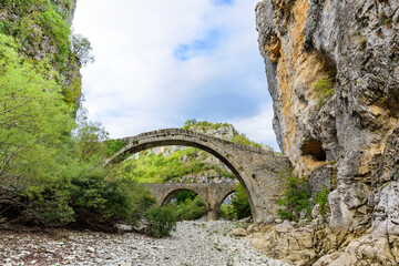 Fototapeta na wymiar Bridge of Kokkoros or Noutsos. The stone bridge with unique arch was first built in 1750. The bridge spans river of Vikos, just where narrowing in the river by two large rocks takes place.