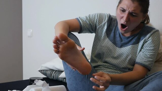 Moisturizing foot mask for dry heels. A woman in a mask on her legs lies on the diva and uses the phone. Self-care during the period of the virus at home