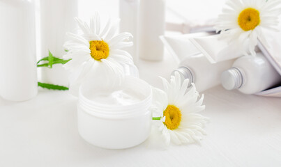Obraz na płótnie Canvas Moisturizer skin cream in white jar with chamomile flowers. Mockup white plastic jar for moisturizer skin cream, lotion on white background. Set of white skin care products in tubes and bottles