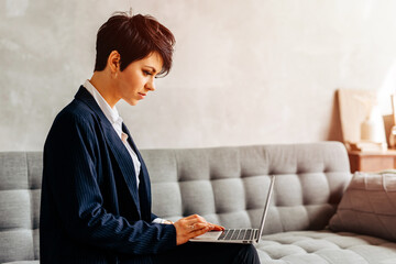 Beautiful business smiling woman sitting on the sofa with a laptop
