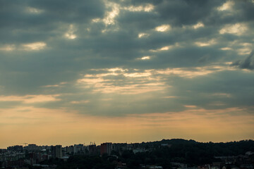 beautiful sunset with fluffy grey clouds on dramatic sky above cityscape silhouettes