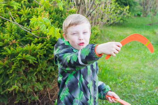 Baby boy blond European holding two orange boomerangs. The child wants to launch bright boomerangs into the sky.