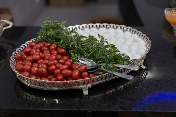 Vasilha de vidro com tomates, manjericão e ovos de codorna, em mesa de buffet.