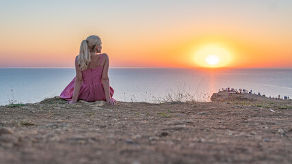 A young girl looks at the sunset stands to the sun face in the summer evening