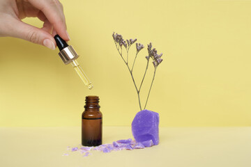 small cosmetic bottle with oil or serum and female hand holding pipette with soup and flower on yellow background 