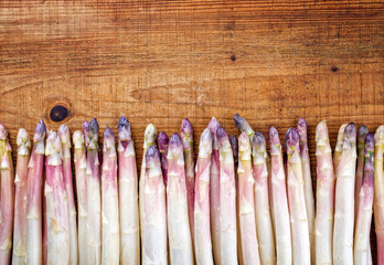 Raw white asparagus with violet head beaded in a row offered as close-up on a wooden background...