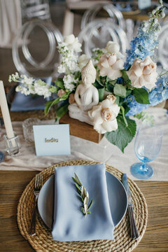 Blue wedding decor. Festive table decorated with flowers on the center, candles, silverware and plates with silk napkins on dusty blue tablecloth