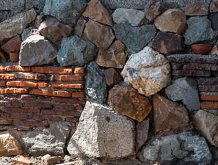 A mosaic of stones and bricks. The wall is made of natural boulders and pebbles. Texture from natural materials. Colorful background. Day Sunny. Georgia.