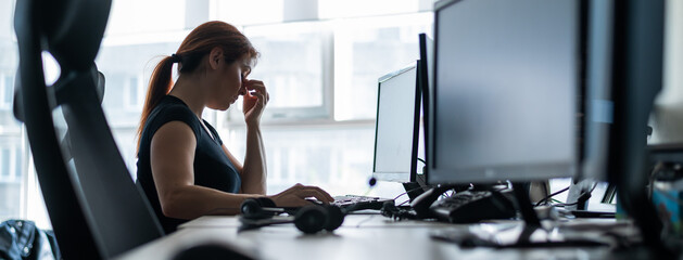 Tired woman workaholic t-shirt works in an empty office and holds fingers on the bridge of the...