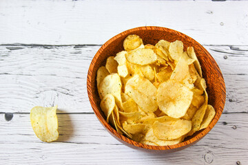 Potato chips or crisps in wooden bowl against white wooden background. Pile of potato chips. Potato...