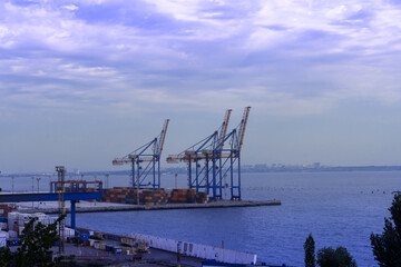 Seaport area, large cranes and stacked shipping containers against the backdrop of the sea
