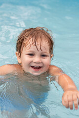 Fototapeta na wymiar a smiling two-year-old boy swims in a pool 