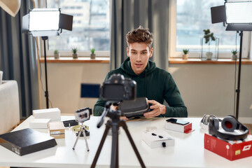 Young male technology blogger recording video blog or vlog review of new vr glasses, headset and other gadgets at home studio. Blogging, Work from Home concept