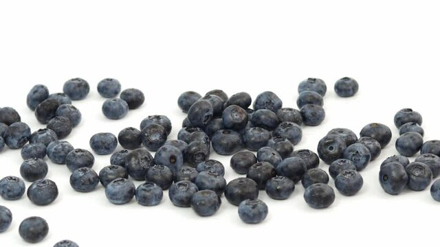 A handful of blueberries are added by womans hand to the pile on the table, white background.