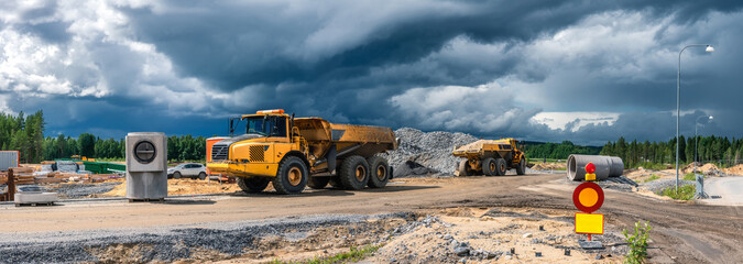 Panorama view on two heavy industrial yellow dump trucks parked close to construction site with...