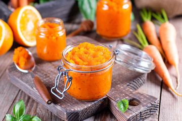 Carrot Jam with orange juice in a glass jar on a wooden table, ingredients on a wooden board