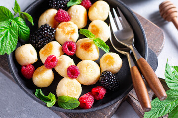 Lazy dumplings of cottage cheese with raspberries, blackberries, mint on light concrete background.