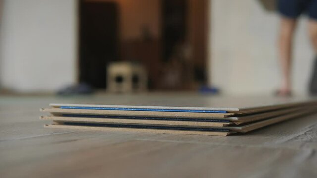 The master lays the laminate in the apartment. Close-up a stack of laminate is lying on the floor in the apartment, the master takes a bar of laminate and puts it on the floor.