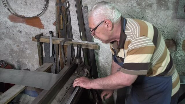 An older man working with sheet metal in his workshop. A worker works carefully with sheet metal