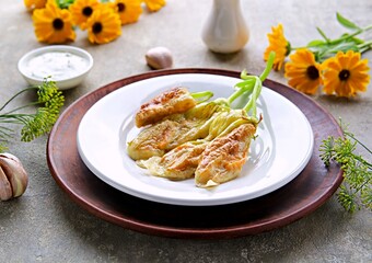 Hot appetizer, deep-fried zucchini flowers, on a white plate on a gray concrete background.