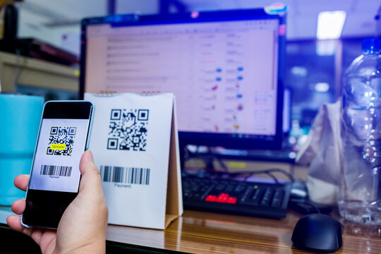Selective focus to customer hand holding smart phone to scan Qr code payment and barcode with blurry online shopping website on computer screen. The concept of digital payment and online shopping.