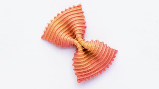 Colored bow tie pasta. Closeup single orange farfalle on white background.