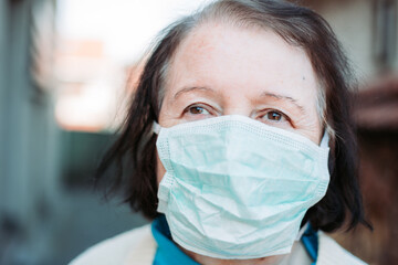 Outdoor photo of elderly woman wearing protective, surgical mask.