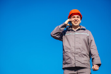 Construction worker in a helmet against the blue sky talking on the phone. Contractor control...
