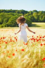 Beautiful young woman in white dress walking in poppy field on a summer day