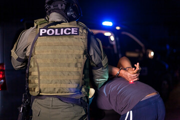 A police officer puts handcuffs on a criminal's hands during an arrest. Police car with flashing lighthouses. Blurried