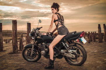 beautiful brunette girl in denim shorts and leather boots sits on a motorcycle on the dead sea summer
