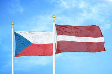 Czech and Latvia two flags on flagpoles and blue cloudy sky