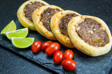 Delicious Lebanese food, genuine sfihas on a slate plate with tomatoes and lemons.
