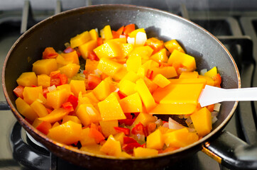 Pieces of ripe orange pumpkin are fried in pan with vegetables